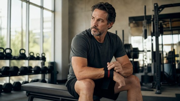 Man sitting on a workout bench in a gym.