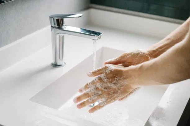 Close-up photo of man washing his hands at a bathroom sink.
