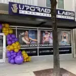 exterior of a storefront with an Upgrade Labs sign and a purple and yellow balloon arch
