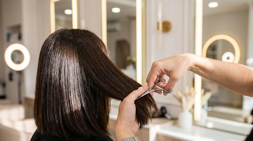 Ahk Cu Post Hairdresser cutting woman's straight brown hair in salon with bright lighting